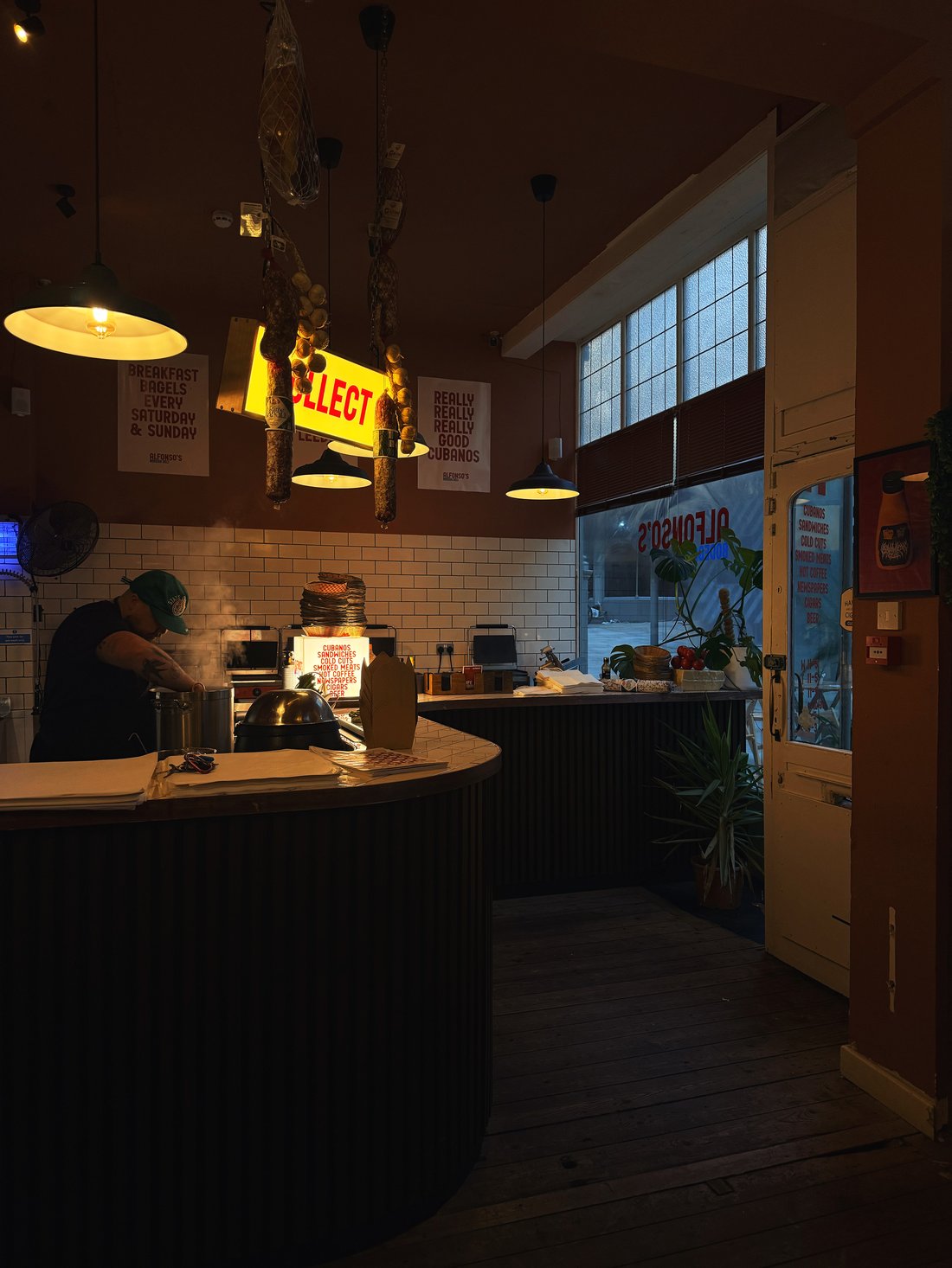 Inside Alfonso's in the evening, with hanging salami and the Really Really Really Good Cubanos poster